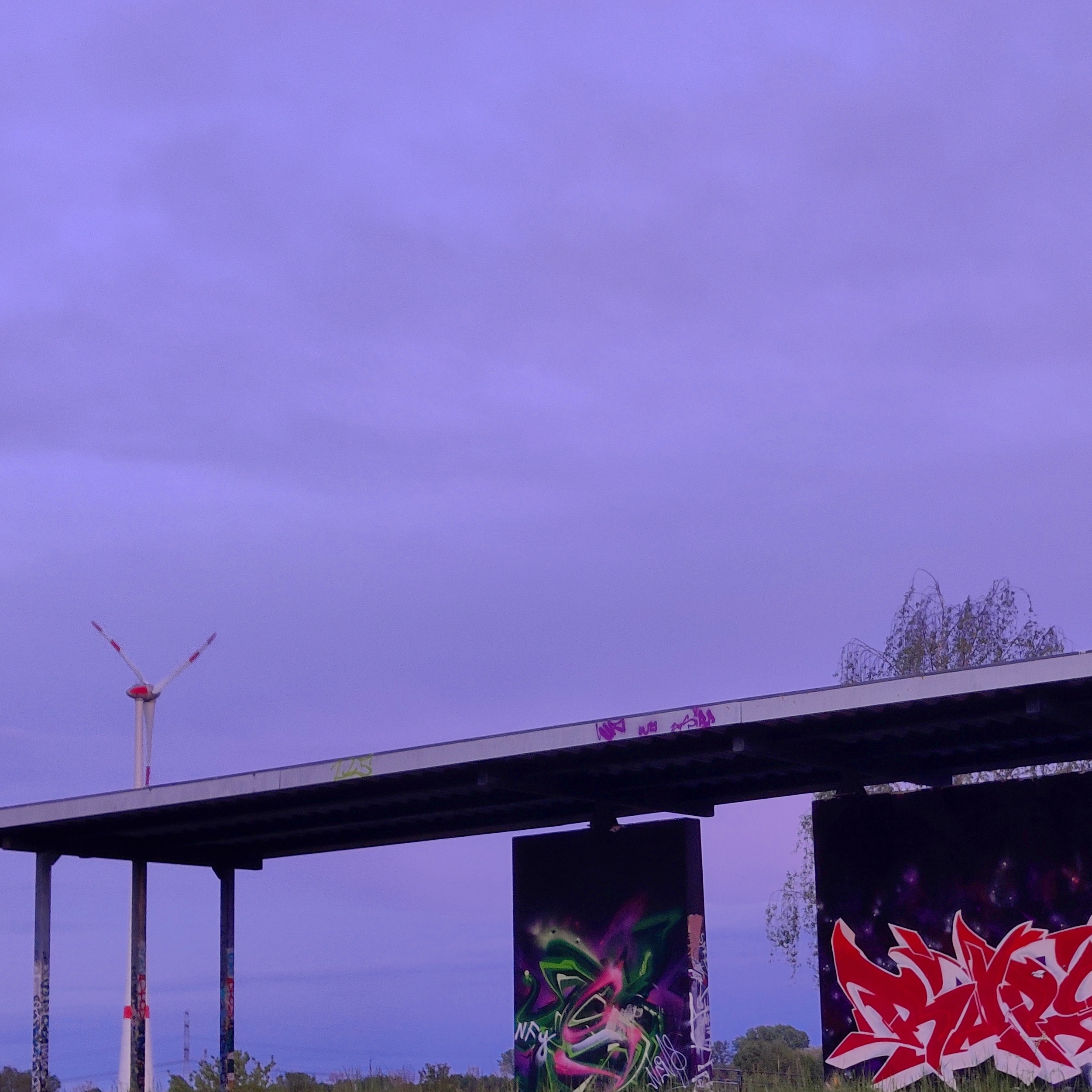 photo of a concrete roof with some walls beneath it in front of a dark-blue sky past sunset. the concrete is covered in graffiti, a wind turbine is peeking out from behind the roof on the left side
